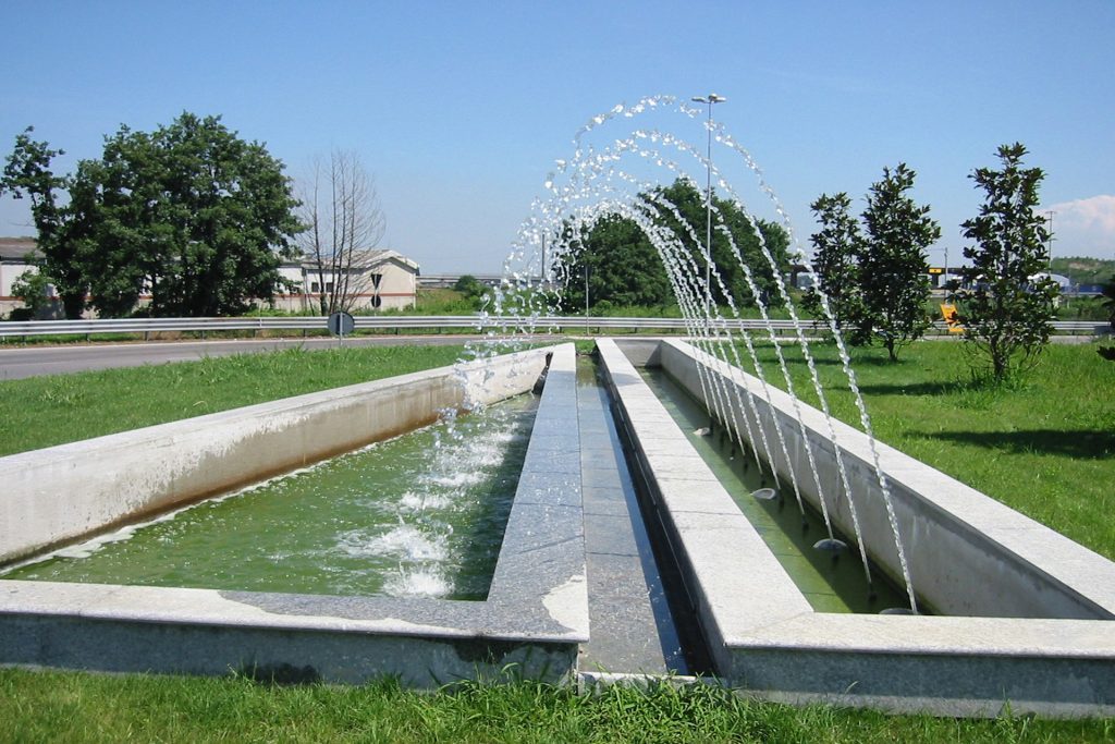 Modern artistic fountain with water jets and greenery